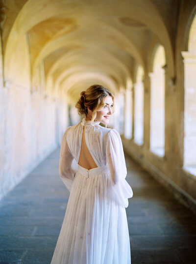 Stunning bride looks over her shoulder in wedding gown in arched hallway