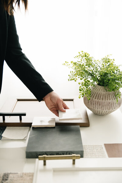 A women in a black blazer places a white tile sample on her desk