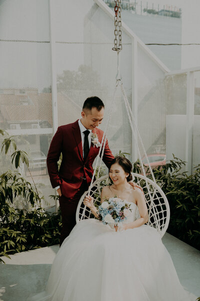 bride sit on swing and groom standing