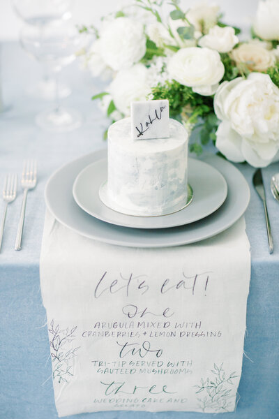 Reception table setting with small guest cake and customized wedding naptkins