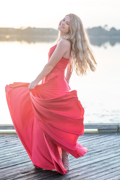 High school senior girl in red dress spinning on boardwalk over a lake by Khim Higgins Photography.