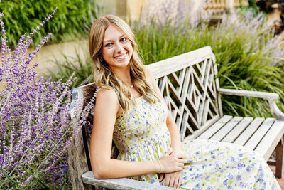 beautiful high school girl in green and purple floral dress sitting on a bench smiling for her Green Bay senior photography session