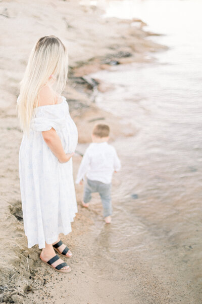Image of expecting mother standing by the water watching her young son play in the water taken by Sacramento Newborn Photographer Kelsey Krall Photography
