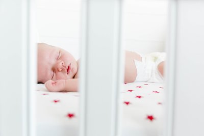 A close-up view through white crib bars showing a peaceful sleeping newborn on a bed with star-patterned sheets.