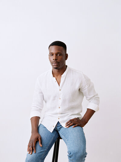 Man poses for photo in white shirt and sitting on stool