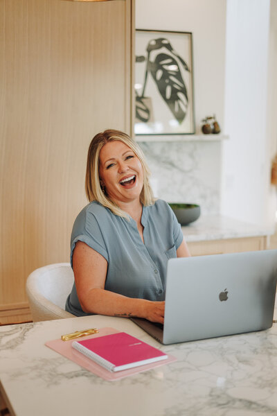 Business coach Melanie Greenough laughing and sitting at a table with a laptop