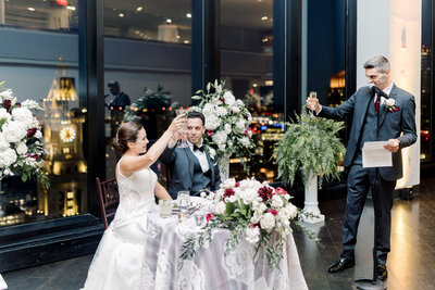 Bride and groom raise glasses for a toast at their Boston State Room wedding reception