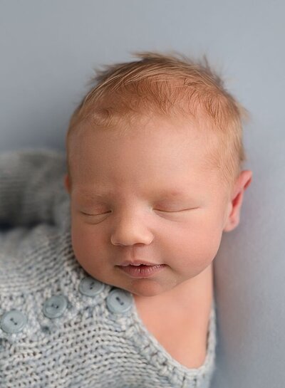 newborn baby boy, wearing blue romper, smiling