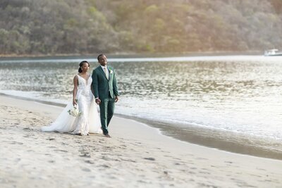 a bride and groom take a stroll on a beach