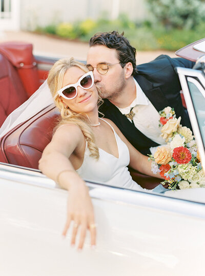 Bride and groom sit in a red and white classic car at the addison grove in texas