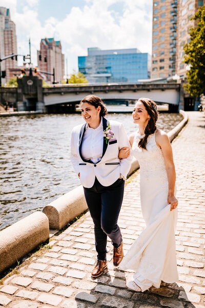 A photo of two brides walking along the Providence River in Waterplace Park in Rhode Island on their wedding day