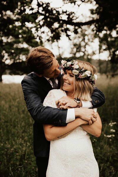 brudgum kramar om brud bakom som bär blomsterkrans under deras midsommarbröllop
