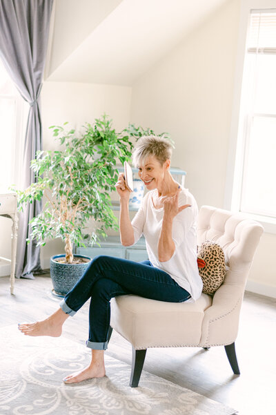 Brand photo of women sitting in chair with legs crossed holding her phone and smiling