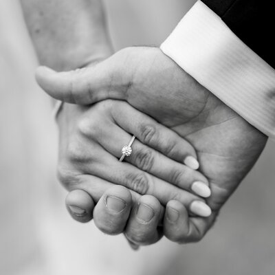Black and white photo of a bride and groom holding hands showing off her engagement ring at their Brigalias wedding