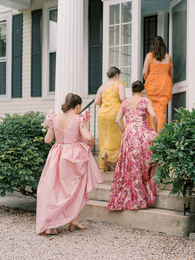 Bridesmaid in pink, yellow, orange dresses walking up stairs