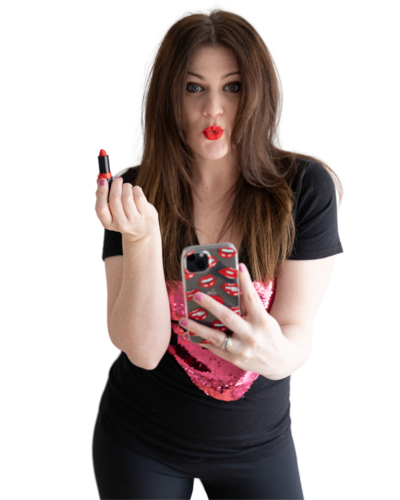 Emily wearing black leggings and a black shirt with a sparkly pink heart that says pink on it. She is holding a phone with red lip pattern all over it and in the other hand is holding a red lipstick tube. She is wearing red lipstick on her lips and is making a kissy putting face with a surprised look on her face.