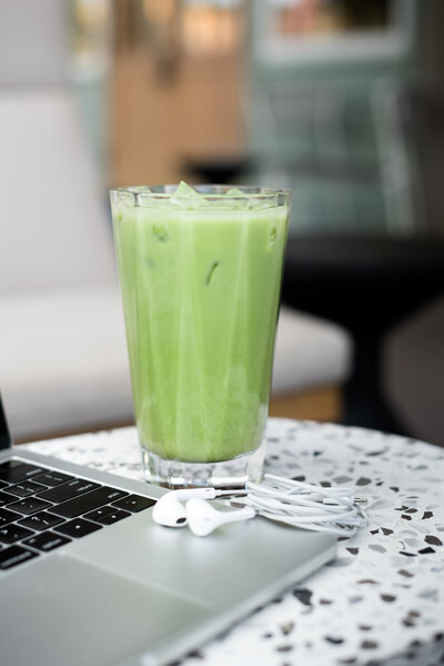 Matcha latte in a glass sitting on a marble table next to a computer