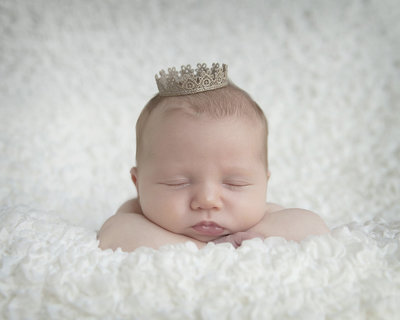 Newborn baby sleeps on fluffy white blanket with crown on head