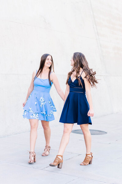 Twin senior girls holding hands and laughing in blue dresses