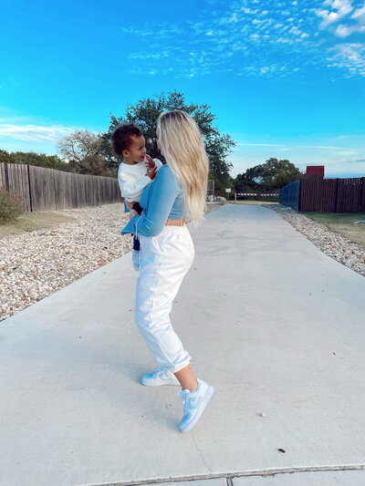 Iskra is holding her toddler, wearing a top that matches the blue sky in the background.