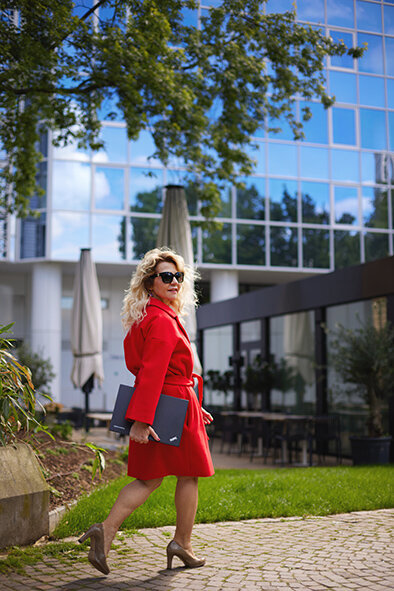 Roxana, a market researcher, walking in a red coat, with a laptop in hands through uptown Frankfurt