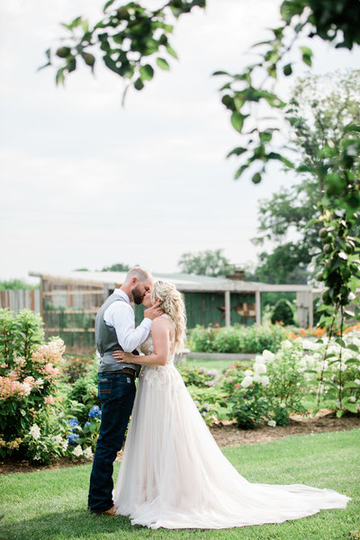 Bride and Groom Kissing in Flower Garden in Summer Wedding at Wild Wood Family Farms