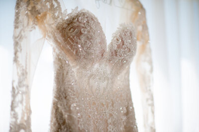 A beaded lace bridal gown hanging in a window
