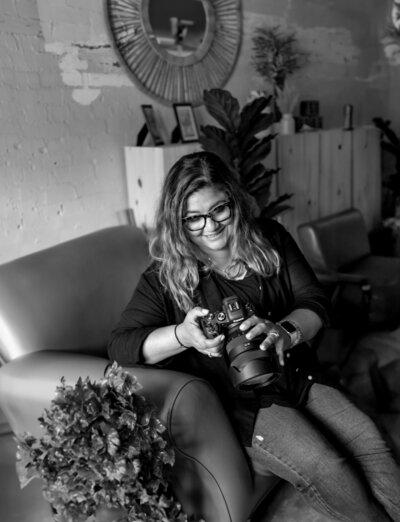 photographer sitting on a couch in a home looking at her camera smiling