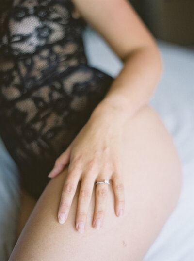 Boudoir image of woman leaning on bed with hand resting on leg