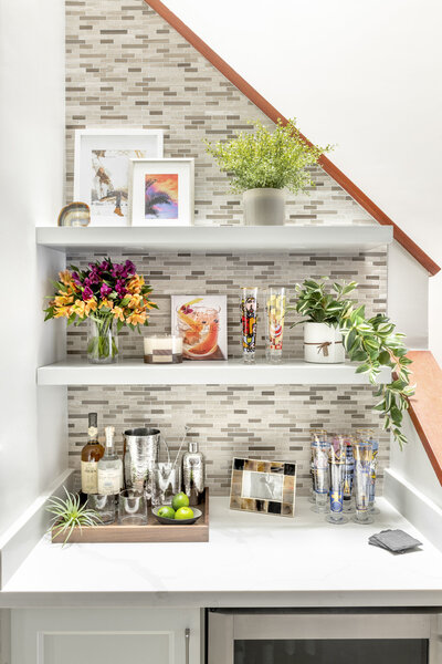 Home bar styled with elevated barware, plants, candles, art, decorative accessories, drink glasses and coasters