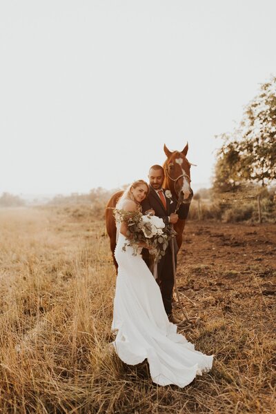 bride and groom posing next to a horse