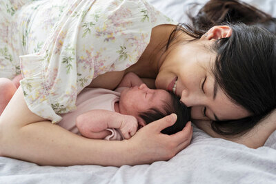 New mother and baby daughter cuddling together on bed at home in Surrey