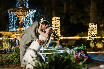 Groom dips bride in front of lit up fountain at night, Savannah Weddings