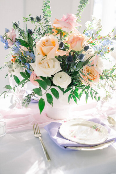 pastel pink, green, and purple floral centerpiece in front of wedding reception place setting