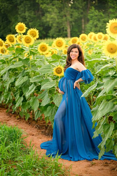 expectant mother in blue dress standing in a sunflower field in charlotte area