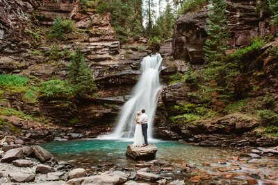 Elopement couple stands by a creek with a mountain in the background in Ouray Colorado