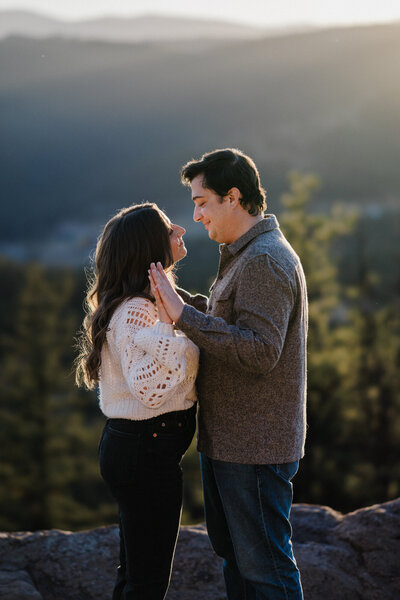 Man and woman stand on mountain overlook during engagement photos,