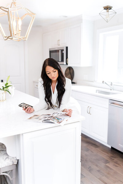 realtor in kitchen looking through a magazine with her cell phone