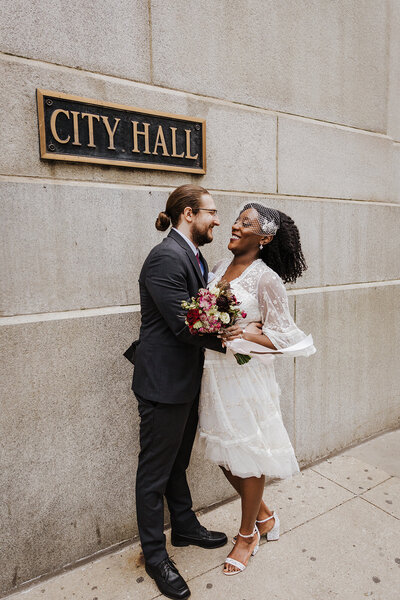 couple is standing by city hall sign and embracing and laughing
