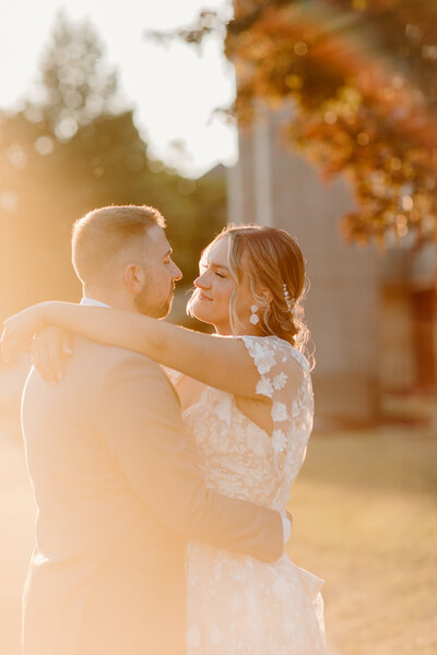 bride and groom with arms around each other at sunset