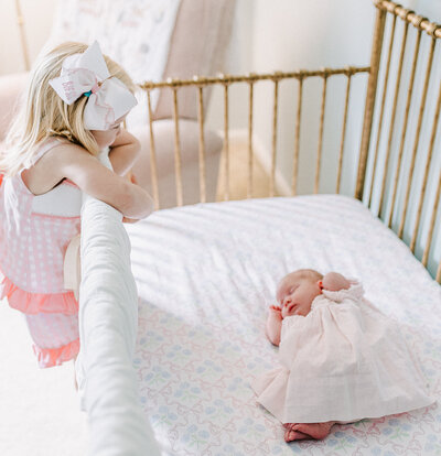 A sweet baby girl gazes gently from her crib, wrapped in cozy textures with delicate details, reflecting a warm and serene lifestyle newborn session.
