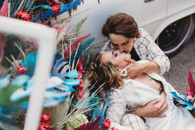 Weddig photo session of bride and groom sitting on ground in front of car kissing