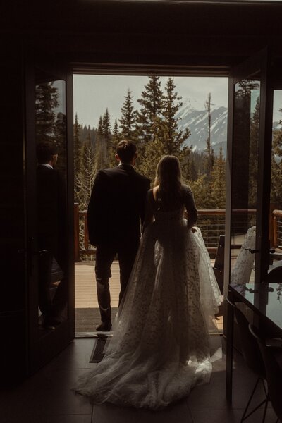 A Couple walking out of their Colorado AirBnB to a mountain view  as they face away from their Colorado wedding photographer.