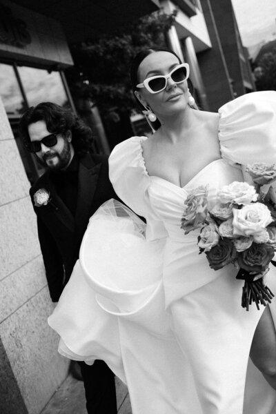 Black and white photo of a bride and groom in sun glasses walking through Dublin. 