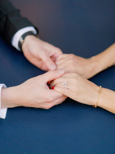 a man and woman holding hands  on top of a blue table with a diamond ring and bracelet showing