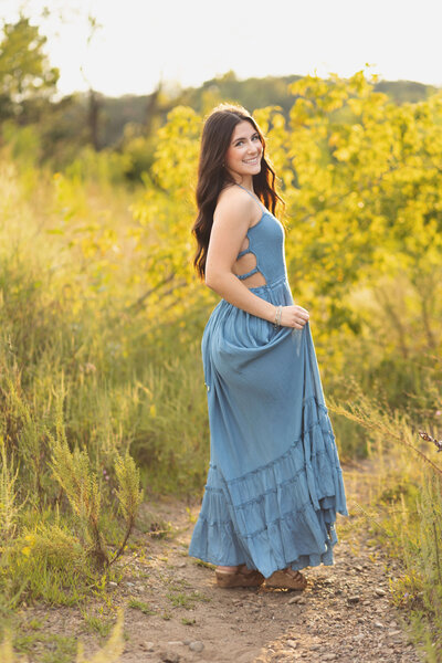 Senior girl in blue dress in grassy field at sunset