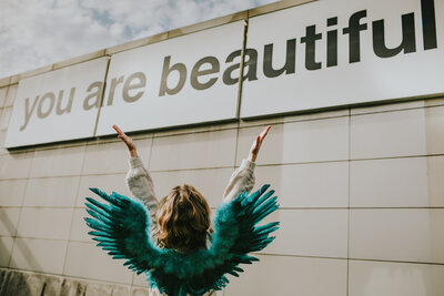 woman wearing teal wings holding arms up