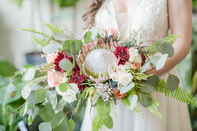 Bride holds stunning bouquet filled with colorful flowers and large protea