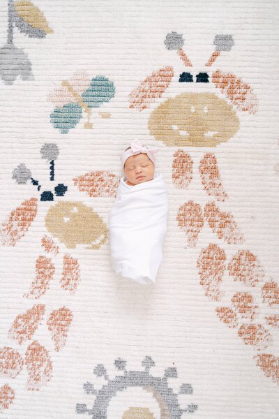 Newborn baby swaddled up on her rug with giraffes