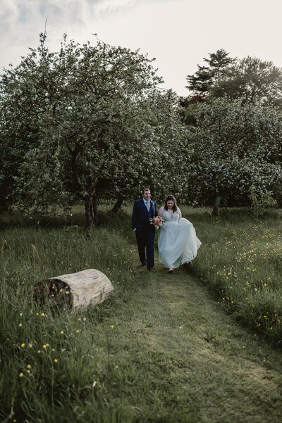 bride and groom walking through a meadow